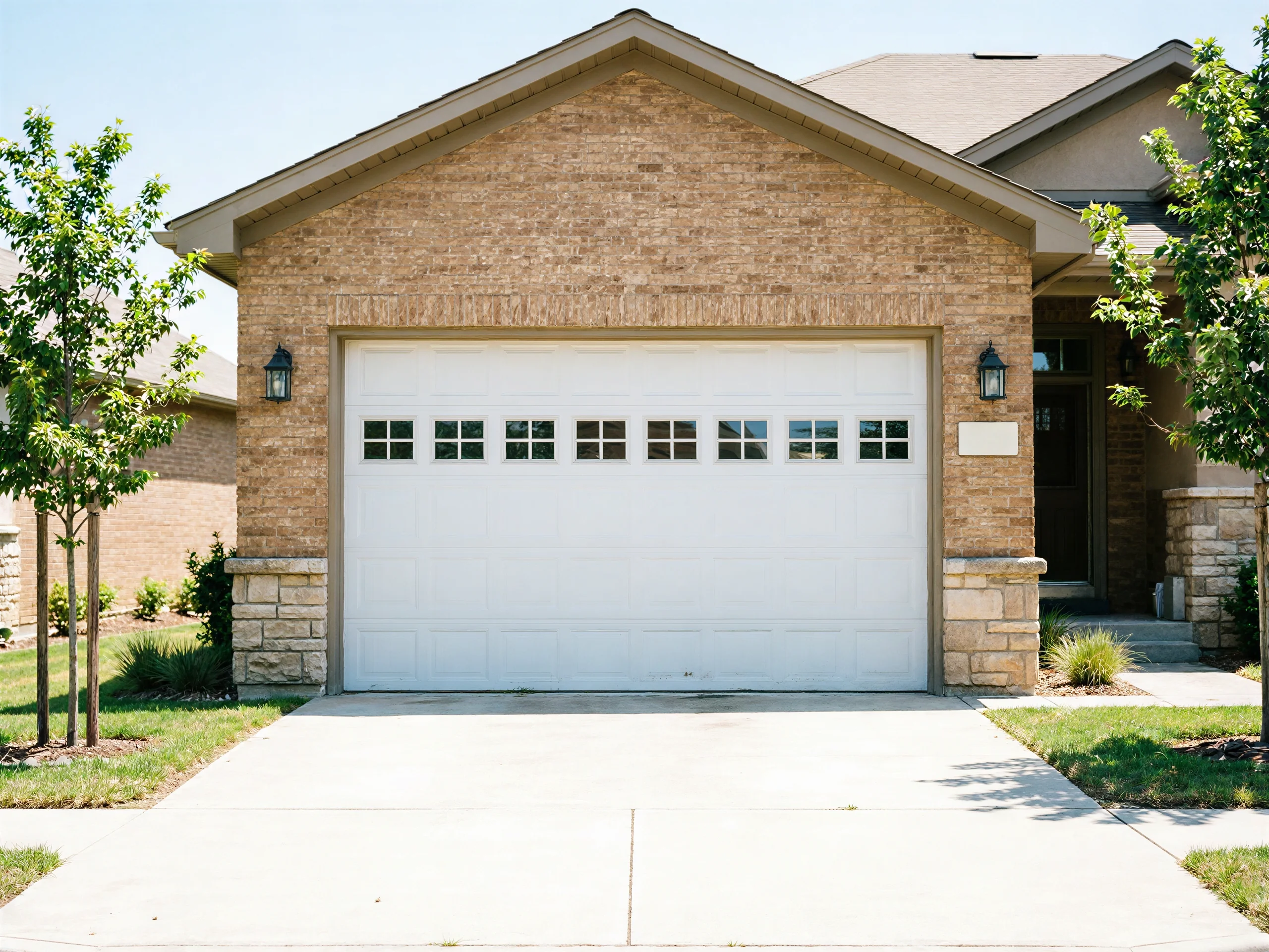 A white garage door with windows on a brick house with a concrete driveway.